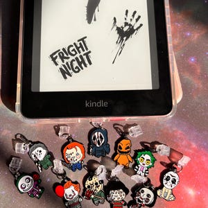 May include: A Kindle e-reader with a clear case displaying the words "FRIGHT NIGHT" and various spooky graphics. Below are several horror movie character charms, including Jason Voorhees, Chucky, and Pennywise.