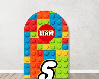 May include: A colorful backdrop for a birthday party, featuring a pattern of red, blue, yellow, and green Lego bricks. The backdrop is shaped like an arch and has a white number "5" and a red circle with the name "Liam" in white letters.