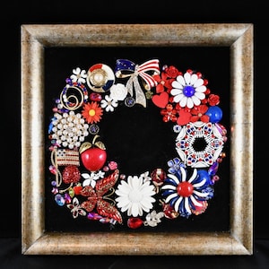 Pode incluir: Uma grinalda decorativa composta por vários broches e enfeites vermelhos, brancos e azuis, dispostos em um padrão circular. A grinalda está definida contra um fundo preto dentro de uma moldura dourada. O design inclui elementos florais e patrióticos.