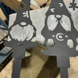 May include: Two black metal garden gnomes with a snowflake design. The gnomes are standing upright and have a whimsical design.