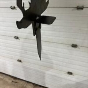 May include: A metal silhouette of a deer with a stake on the back. The stake is inserted into the ground. The deer silhouette is black.