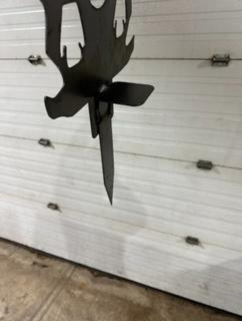 May include: A metal silhouette of a deer with a stake on the back. The stake is inserted into the ground. The deer silhouette is black.