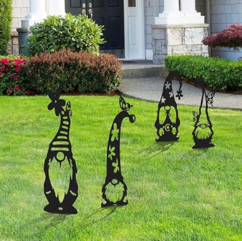 May include: Four black metal garden gnomes with butterfly accents. The gnomes are standing on a green lawn in front of a house.