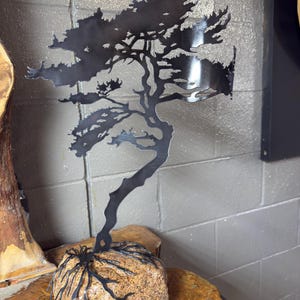 May include: A black metal sculpture of a tree with a brown stone base. The tree is stylised and has a flowing, organic shape. The sculpture is a unique and decorative piece of art.