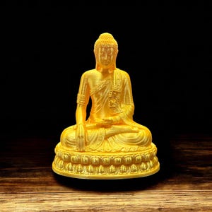 May include: A golden Buddha statue sitting in a meditative pose with hands in lap. The statue is on a base with a decorative design.