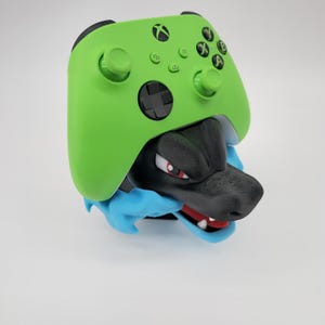 May include: A lime green Xbox controller cover with black buttons and a black and gray dragon head design. The dragon has red eyes and a blue collar. A unique gaming accessory.