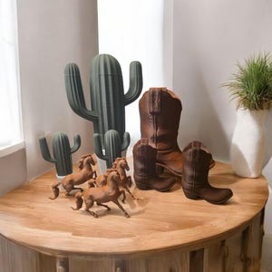 May include: A wooden table with four brown horses, three green cactus plants, and three brown cowboy boots. The boots are all different sizes and styles.
