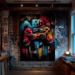 May include: A vibrant, graffiti-style artwork featuring a video game controller. The controller is painted in shades of red, yellow, and orange, with black buttons and a screen. The background is a mix of blue, red, and yellow paint splatters, with graffiti art.