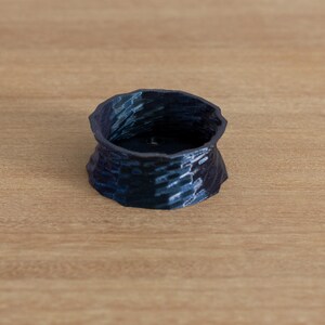 May include: A small, dark blue, ceramic bowl with a textured, wavy design. The bowl is empty and sitting on a light brown wooden surface.