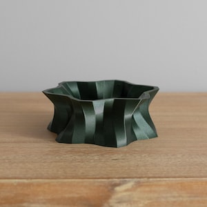 May include: A dark green ceramic bowl with a unique, geometric, star-shaped design. The bowl has a smooth, matte finish and is perfect for displaying small items or serving snacks.