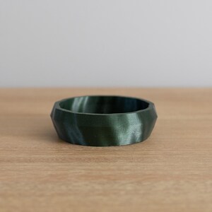 May include: A small, dark green and blue geometric bowl with a textured surface. The bowl is made of a smooth, hard material and has a slightly rounded shape.