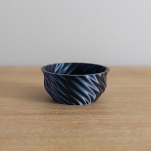 May include: A small, dark blue bowl with a swirling, textured pattern. The bowl is made of ceramic and has a rounded shape.