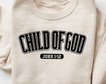May include: A beige sweatshirt with the text "CHILD OF GOD" in black with a black outline. Below the text is "JOHN 1:12" in black.