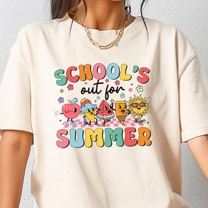 May include: A cream coloured t-shirt with a graphic print of cartoon characters celebrating summer. The text on the shirt reads "School's out for Summer".