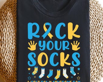 Pode incluir: Camiseta preta com o texto "Rock Your Socks" em letras amarelas e azuis. O texto é rodeado por meias amarelas e azuis e as palavras "World Down Syndrome Day".
