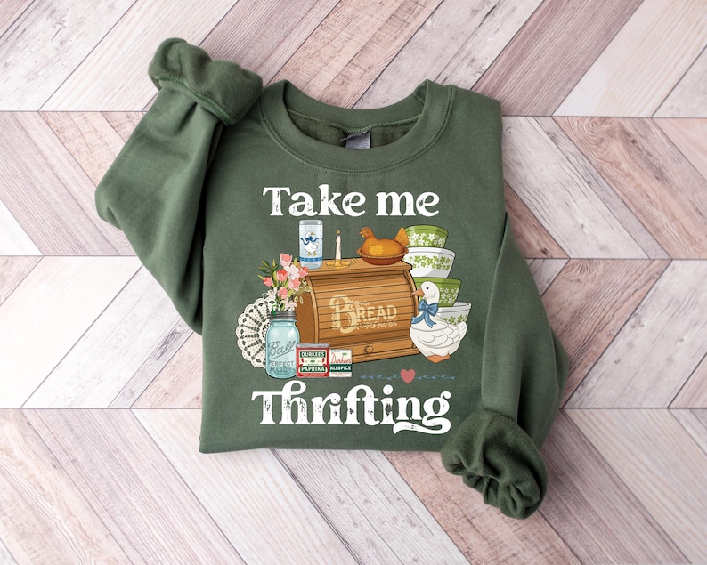 May include: Green sweatshirt with the words "Take me Thrifting" and a graphic of a bread box, bowls, and a duck. The sweatshirt is a solid green color with a crew neck and long sleeves.
