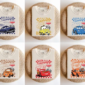 May include: Six beige t-shirts with car graphics. Each shirt displays a different cartoon car design, including names such as "Hudson", "Luigi", "Sally Carrera", "Tow Mater", "McQueen", and "Snot Rod", and checkered flags.