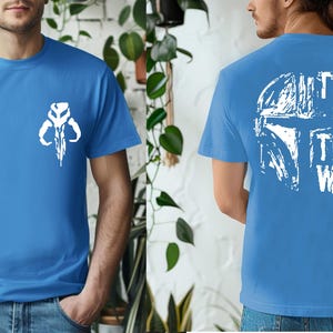 May include: A blue t-shirt with a white graphic of a skull-like symbol on the front and a helmet design with the text "THIS IS THE WAY" on the back. The shirt is short-sleeved and made of a soft material.