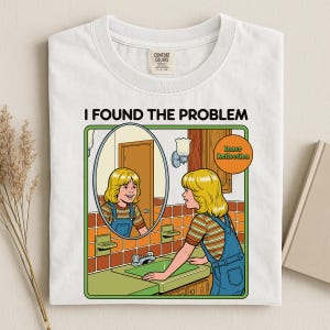 Könnte beinhalten: Ein weißes T-Shirt mit einer grafischen Illustration einer Person mit blonden Haaren, die eine blaue Latzhose und ein gestreiftes Oberteil trägt und an einem Waschbecken steht. Der Text lautet I FOUND THE PROBLEM und Inner Reflection. Label sichtbar.