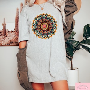 May include: A light gray t-shirt featuring a vibrant, detailed mandala design in shades of red, yellow, blue, and green. The mandala is centered on the shirt. The shirt is a casual, oversized style.