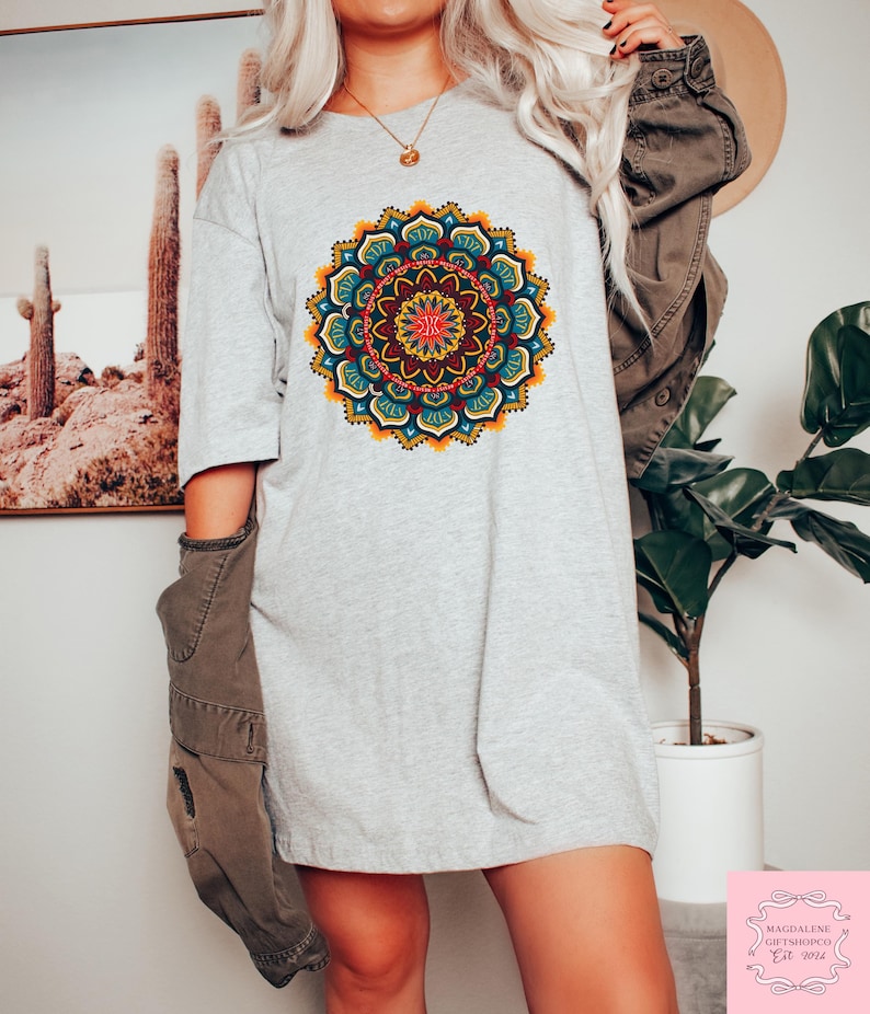 May include: A light gray t-shirt featuring a vibrant, detailed mandala design in shades of red, yellow, blue, and green. The mandala is centered on the shirt. The shirt is a casual, oversized style.