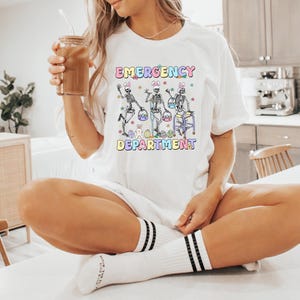 May include: White t-shirt with a graphic of three skeletons holding Easter baskets and the text "Emergency  Easter Department".