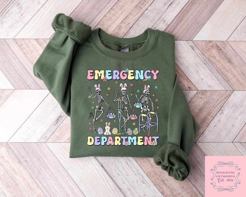 May include: Green sweatshirt with a graphic of three skeletons holding Easter eggs and walking aids. The text "Emergency Department" is written in colorful letters.