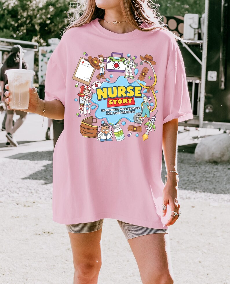 Pu&ograve; includere: Una maglietta rosa chiaro con una grafica colorata che recita "NURSE STORY" con il claim "TO INFINITY AND BEYOND FOR OUR PATIENTS". La grafica include elementi medici e dei cartoni animati. La maglietta &egrave; indossata.