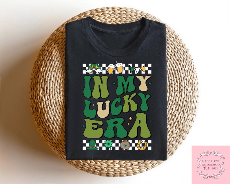Puede incluir: Camiseta negra con un gr&aacute;fico verde, blanco y dorado que dice "In My Lucky Era". El gr&aacute;fico presenta tr&eacute;boles, jarras de cerveza y una herradura.