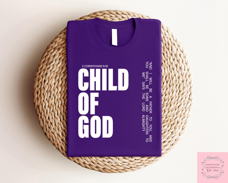 Peut inclure: Un t-shirt violet avec l'inscription "CHILD OF GOD" en grandes lettres blanches. Le texte "2 Corinthiens 6:18" est au-dessus des mots. Le t-shirt affiche &eacute;galement une citation. Le t-shirt est pos&eacute; sur un tapis rond en osier.