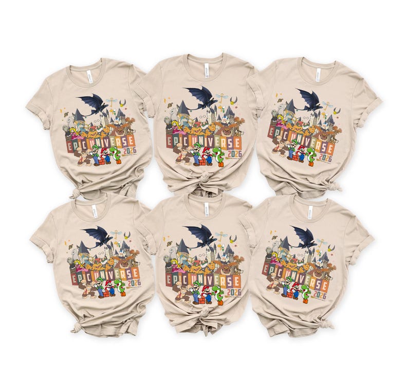 May include: Six beige short-sleeved t-shirts with a colorful graphic design. The design includes a castle, cartoon characters, a bat, and the text "EPIC UNIVERSE 2026". The shirts are neatly arranged.