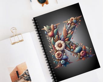 May include: A spiral bound notebook with a black cover featuring a floral design that forms the letter K. The flowers are in shades of blue, pink, yellow, and green.