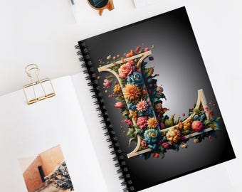May include: A black spiral notebook with a floral design featuring the letter L. The letter is made of flowers in shades of pink, red, blue, yellow, and green.