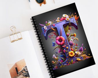 May include: A spiral notebook with a black cover featuring a purple letter "T" surrounded by colorful flowers and leaves. The notebook has a black spiral binding.