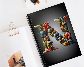 May include: A black spiral notebook with a colorful floral letter N on the cover. The letter is made up of flowers, leaves, and vines in shades of red, blue, green, yellow, and orange.