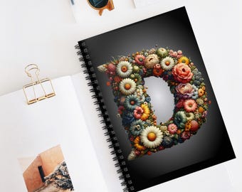 May include: A spiral bound notebook with a black cover featuring a floral letter D. The letter is made up of a variety of colorful flowers, including daisies, roses, and other blooms.