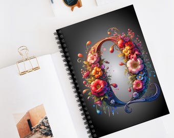 Pode incluir: Um caderno espiral preto com um design floral colorido formando a letra "O". As flores são vermelhas, rosas, laranja, amarelas e azuis.