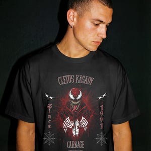 May include: Black t-shirt featuring a graphic of the Marvel Comics character Carnage, with the text "Cletus Kasady" above the image and "Carnage" below. The design includes the year "1991" and spiderwebs.