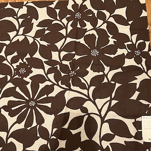 Może przedstawiać: Brązowa tkanina z białym wzorem kwiatowym. Tkanina ma duży wzór kwiatowy z liśćmi i kwiatami. Tkanina jest mieszanką lnu.