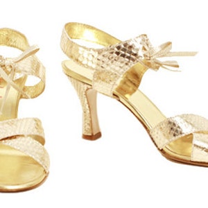 Könnte beinhalten: Ein Paar goldene High-Heel-Sandalen mit Schlangenhautmuster. Die Sandalen haben einen Riemen um den Knöchel und ein Schleifendetail vorne.