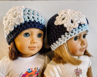 Puede incluir: Dos muñecas con gorros de ganchillo azul y blanco con detalles de flores. Los gorros están hechos con una combinación de hilo azul, blanco y azul claro. Las muñecas tienen el pelo largo y rubio y llevan camisas blancas.