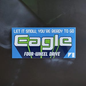 Puede incluir: Una pegatina rectangular con fondo azul y texto blanco y verde. El texto dice "LET IT SNOW, YOU'RE READY TO GO" encima de la palabra "EAGLE" en letras grandes y estilizadas. Debajo, dice "FOUR-WHEEL DRIVE".