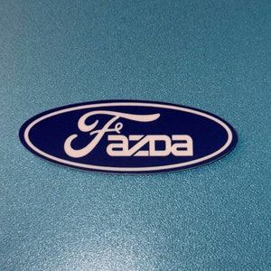 May include: A blue oval sticker with white text that reads "Mazda" in a stylised font.