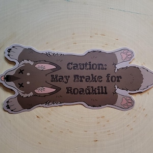 Op de afbeelding: Een grijze en witte cartoon dieren sticker met de tekst "Let op: Kan remmen voor wild".