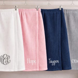 Puede incluir: Cuatro envolturas de spa de tejido de gofre en blanco, rosa, azul marino y gris, colgadas de perchas transparentes. La envoltura blanca tiene un monograma, la envoltura rosa dice "Hope", la envoltura azul marino dice "Taygen" y la envoltura gris dice "Olivia".