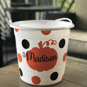 May include: White plastic trick-or-treat bucket with a black and orange polka dot pattern. A pumpkin with the name "Madison" is printed on the front.