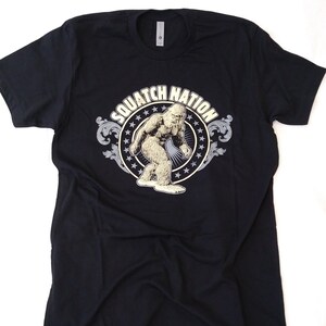 May include: Black t-shirt with a graphic print of a Bigfoot in a circle with the text "Squatch Nation" in a vintage style.