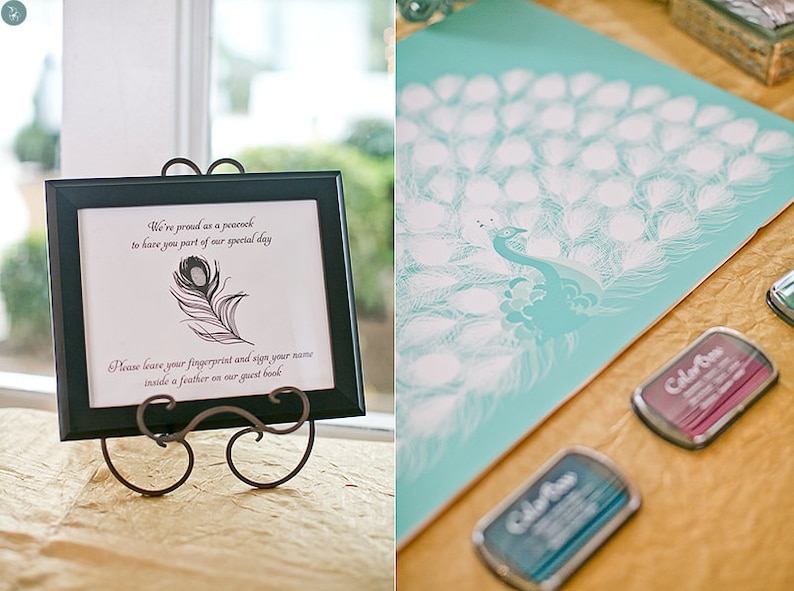 May include: A framed sign with a peacock feather illustration and text, displayed on a decorative stand. The sign reads, "We're proud as a peacock to have you part of our special day. Please leave your fingerprint and sign your name inside a feather on our guest book." A teal peacock guest book and ink pads are also visible.