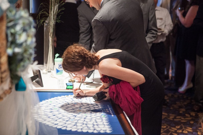 wedding guest signing a peacock guest book poster