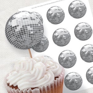 May include: A cupcake topped with white frosting and a silver disco ball cupcake topper. The cupcake topper is a printed image of a disco ball with a silver mirrored finish.